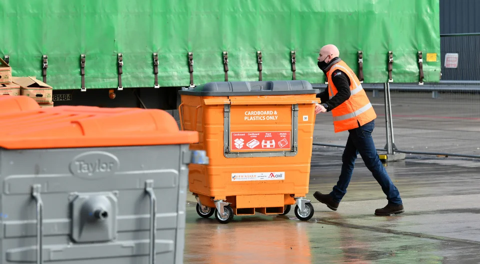 Mark P, Operations Director at Axil, pushing a 1100-litre wheeled bin at a customer site.
