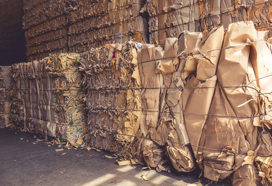 Large bales of compressed cardboard and mixed paper materials stored in a recycling facility.