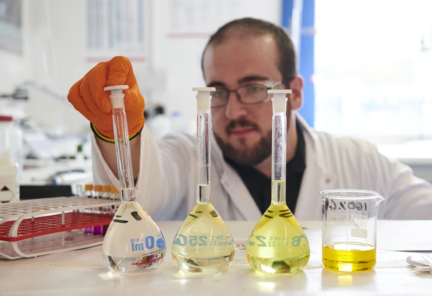 Laboratory technician analysing liquid samples in glass flasks as part of hazardous waste testing.
