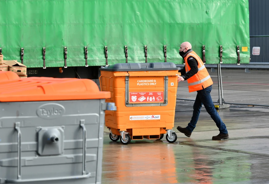 Axil employee moving a commercial recycling bin for cardboard and plastics at an industrial waste management and recycling facility.