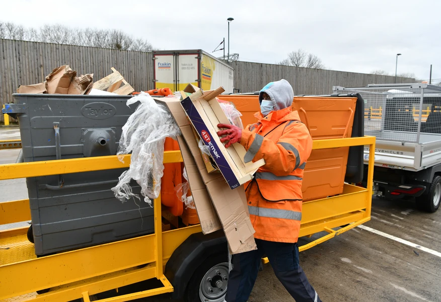 Axil recycling operative collecting cardboard and packaging waste at a resource management facility, demonstrating sustainable waste handling and recycling services.