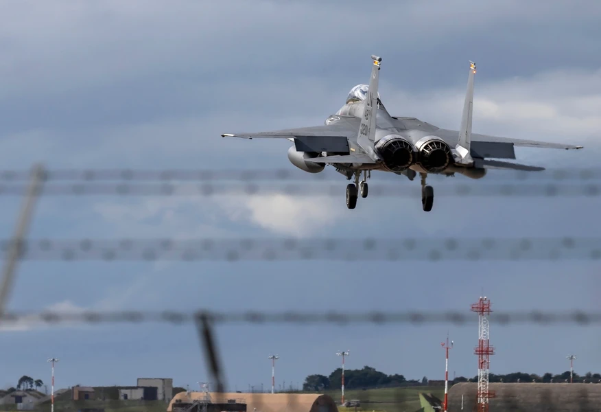 Military fighter jet approaching a runway with landing gear deployed at a defence airbase.