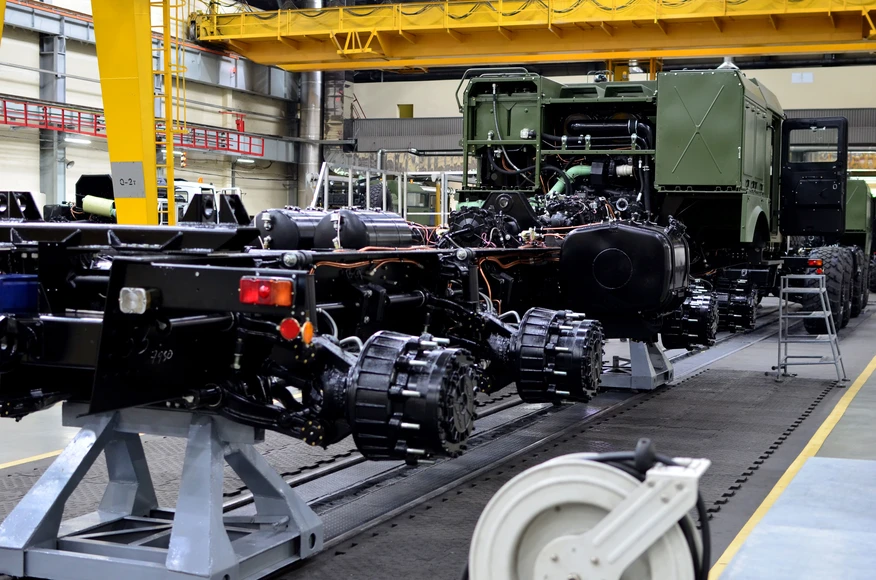Heavy-duty vehicle chassis on an industrial production line, showing drivetrain, axles and mechanical components during assembly in a manufacturing facility.